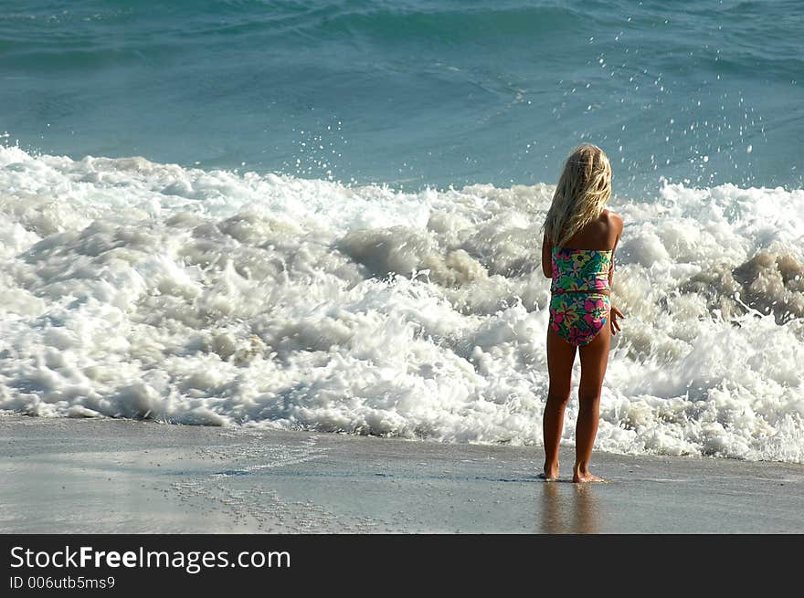 A girl is standing on the sand beach and looking on the waves. A girl is standing on the sand beach and looking on the waves