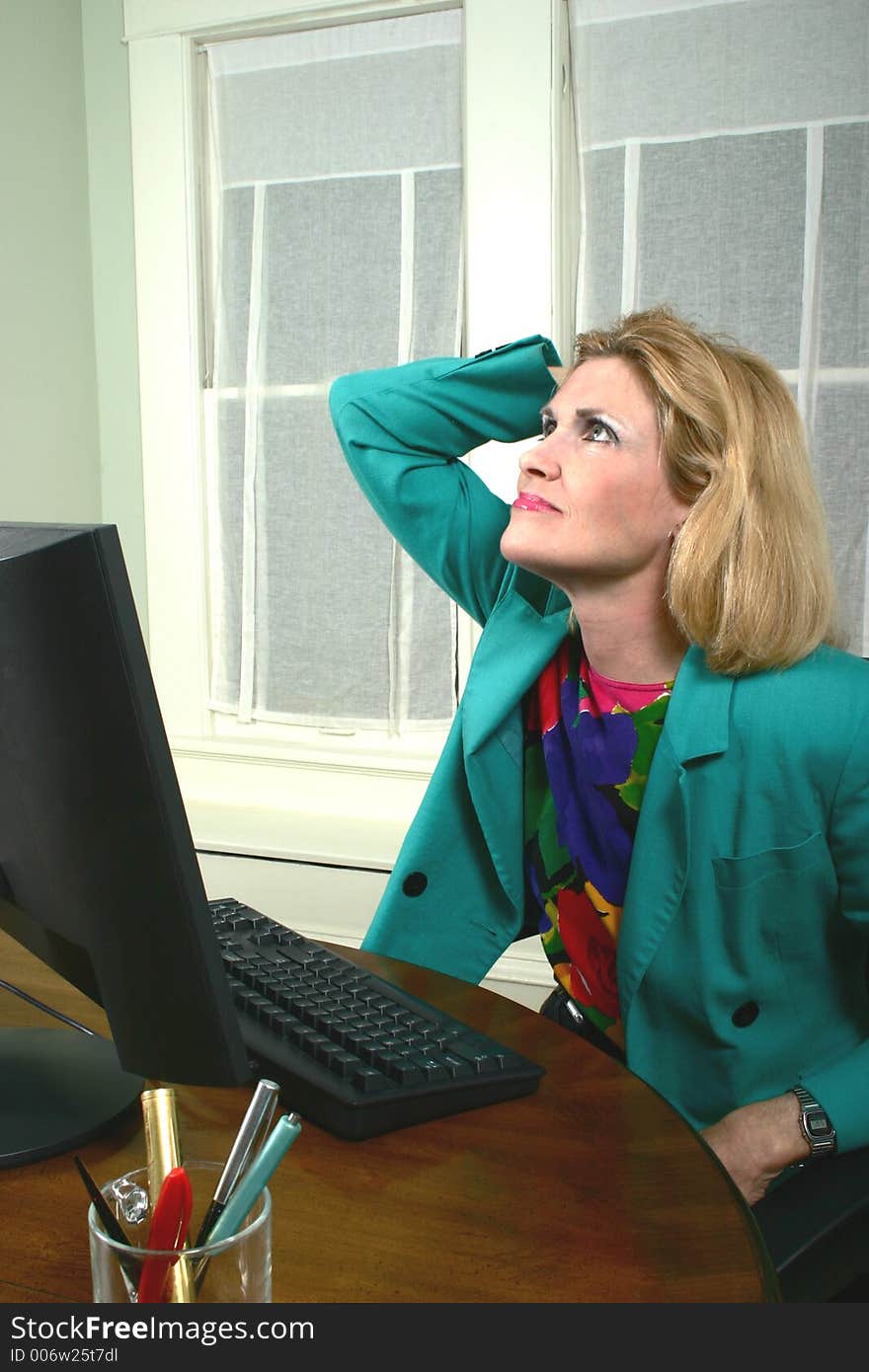 Beautiful middle aged executive business woman with her hand on her head thinking at a computer in the office. Beautiful middle aged executive business woman with her hand on her head thinking at a computer in the office.