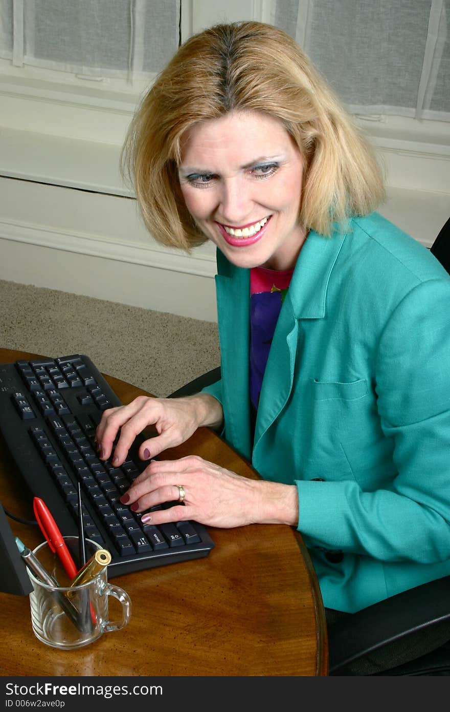 Beautiful middle aged executive business woman looking off-camera and laughing and smiling at a co-worker neighbor while typing on a computer in the office. Beautiful middle aged executive business woman looking off-camera and laughing and smiling at a co-worker neighbor while typing on a computer in the office.