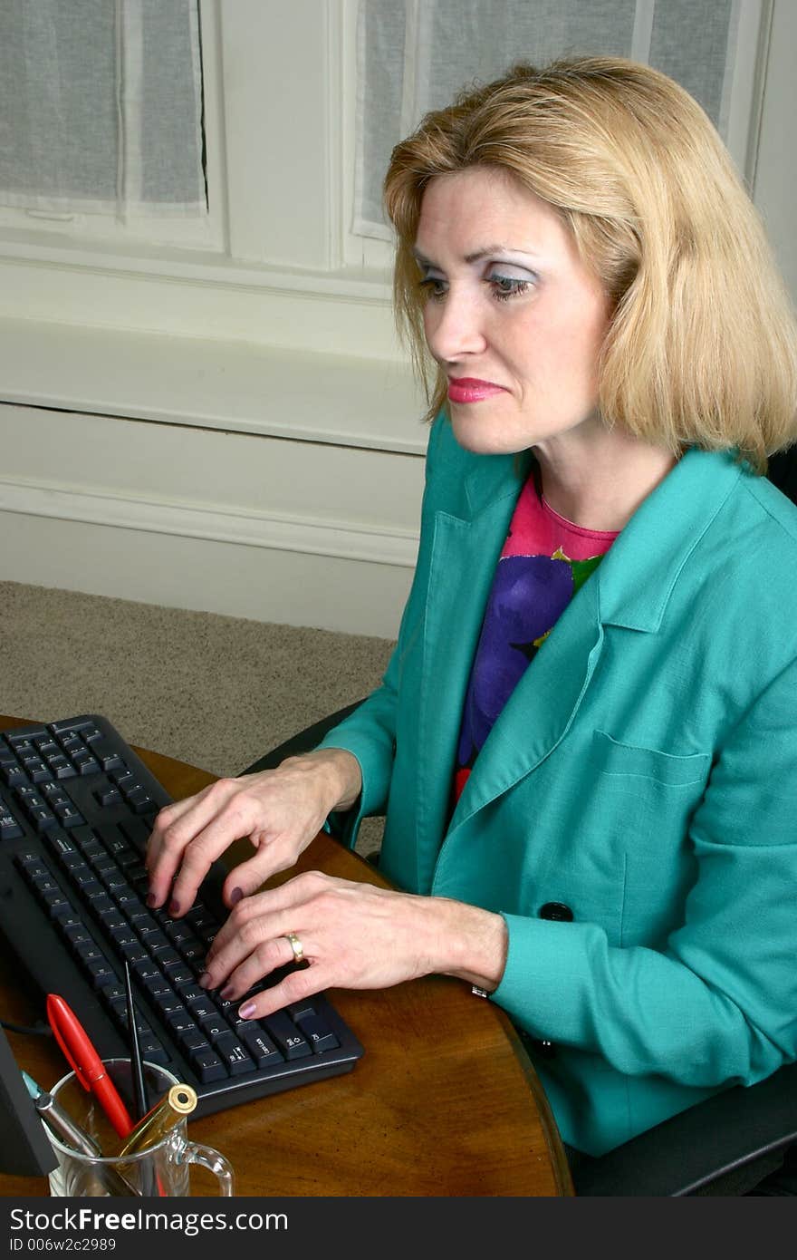 Beautiful middle aged executive business woman with a serious expression typing at a computer in the office. Beautiful middle aged executive business woman with a serious expression typing at a computer in the office.