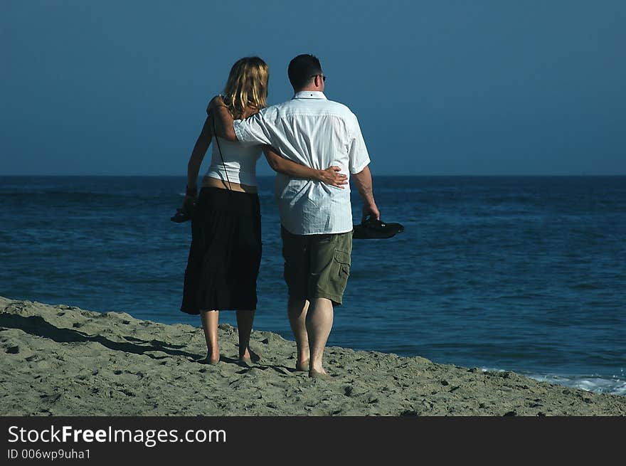 A couple is walking on the beach with sandals in their hands. A couple is walking on the beach with sandals in their hands