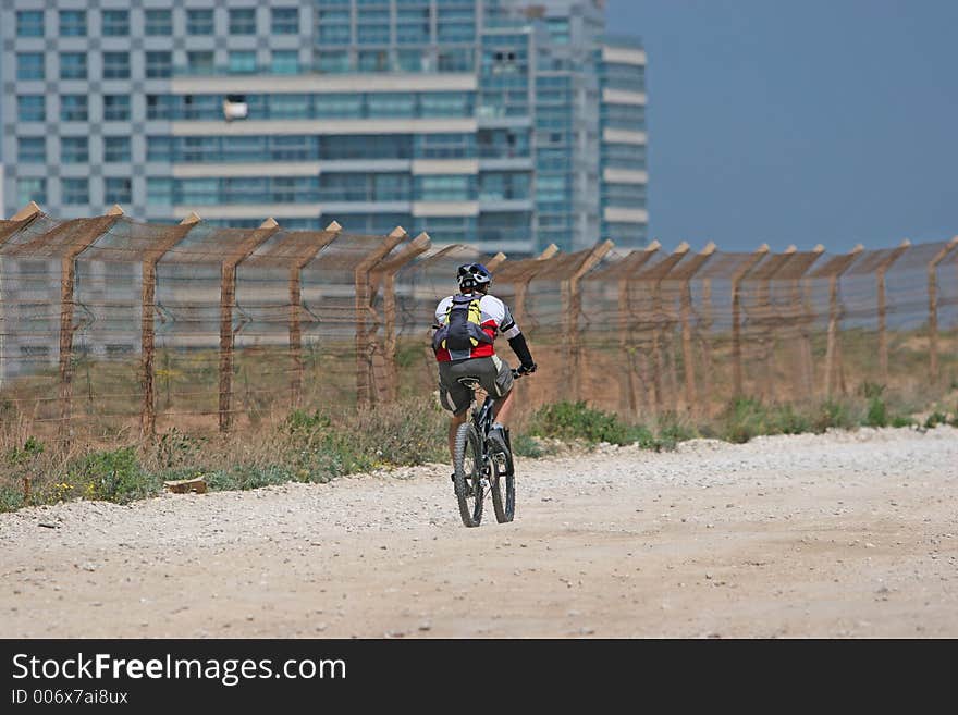 Cyclist riding his bike along a security fence. Cyclist riding his bike along a security fence