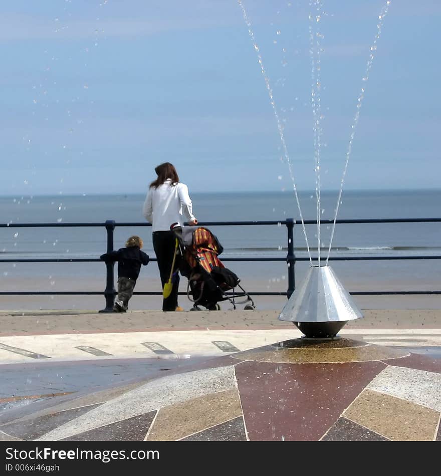 Woman and child look on to beach. Focussed on water in fountain in foreground. Filey, North Yorkshire, UK. Woman and child look on to beach. Focussed on water in fountain in foreground. Filey, North Yorkshire, UK.