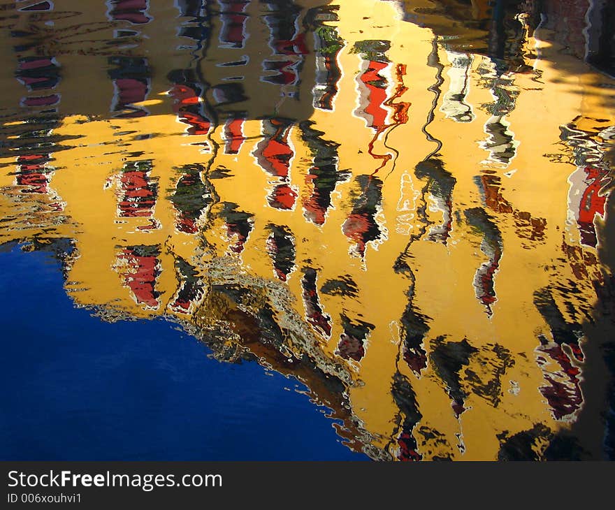 Reflection of yellow building with red window shutters and blue sky on water body. Colours are bright and vivid. Reflection of yellow building with red window shutters and blue sky on water body. Colours are bright and vivid