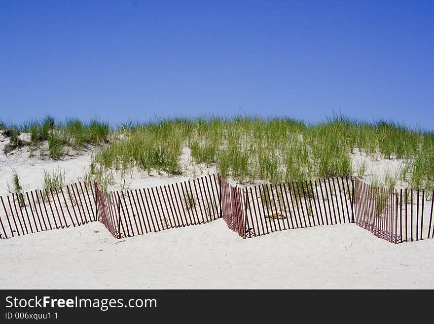 A beach fence zigzags along the dunes protecting it from the weather elements. A beach fence zigzags along the dunes protecting it from the weather elements.