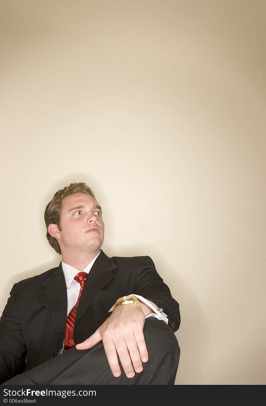 Business man in black suit is holding one leg as he sits crossed legged. Business man in black suit is holding one leg as he sits crossed legged