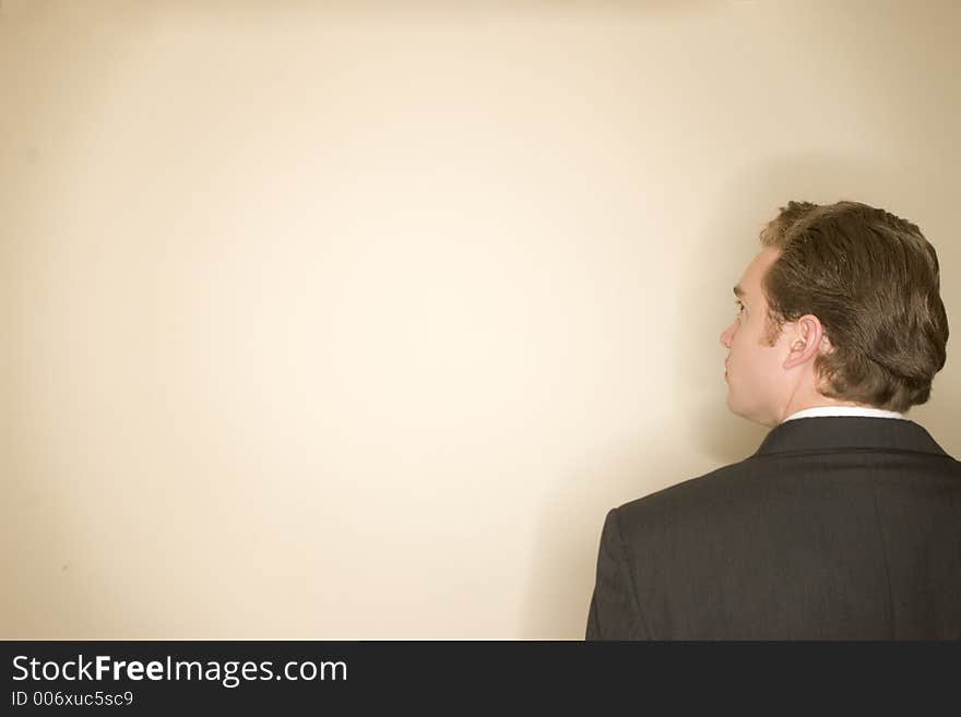 Business man wearing dark suit and white shirt looks away against a tan background. Business man wearing dark suit and white shirt looks away against a tan background