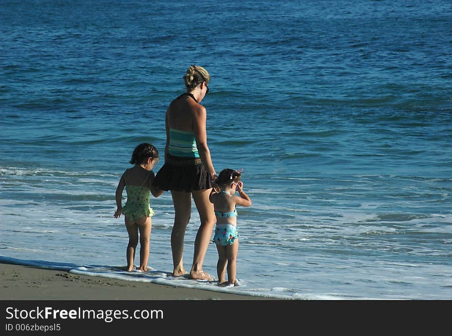 A mom and two daughters standing in the shallow water on the beach. A mom and two daughters standing in the shallow water on the beach