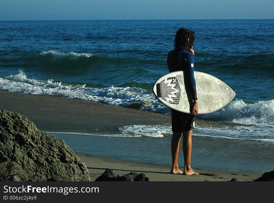 A surfer is standing on the sand beach and waiting for a wave. A surfer is standing on the sand beach and waiting for a wave