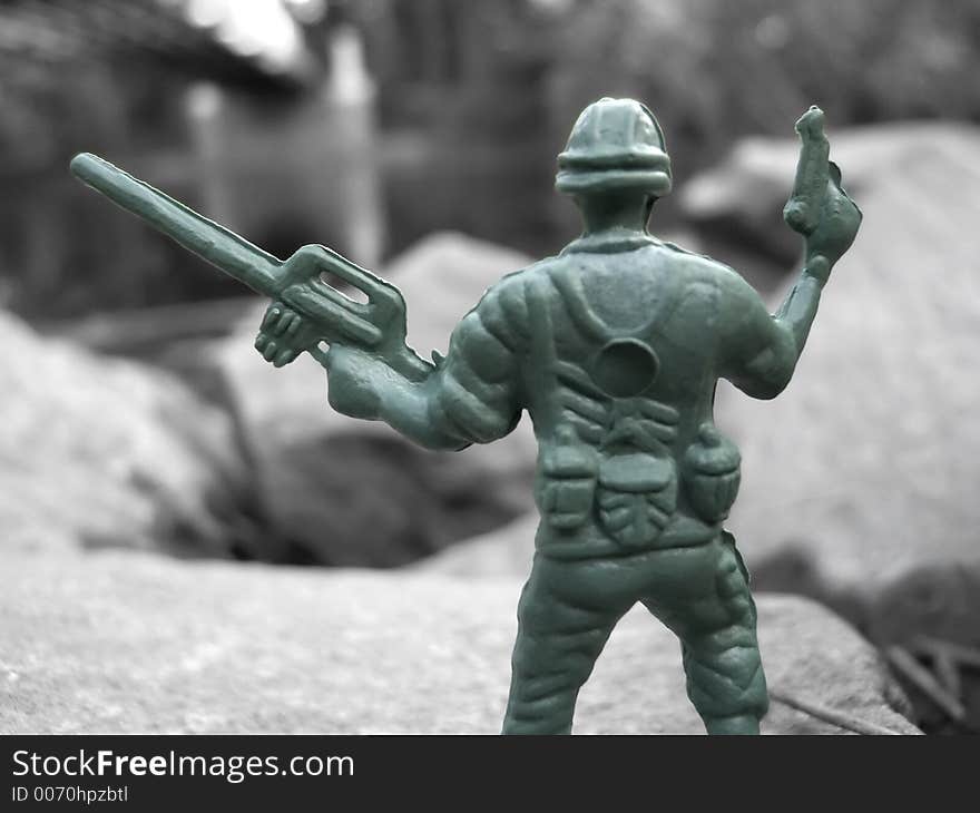 A green plastic army toy soldier in color against a black & white background. A green plastic army toy soldier in color against a black & white background