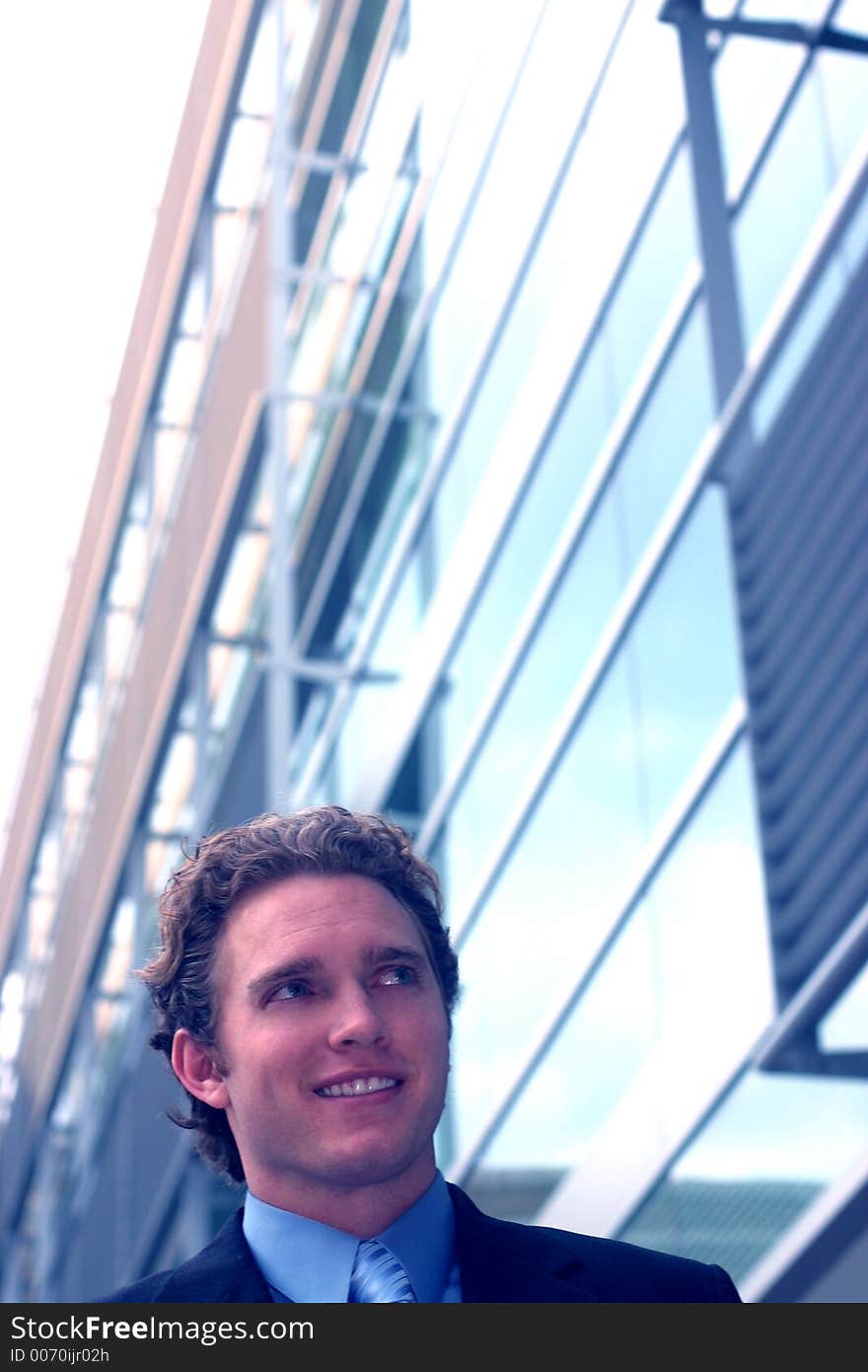 Business man in dark suit, blue shirt, and blue tie smiles in front of large office building. Business man in dark suit, blue shirt, and blue tie smiles in front of large office building