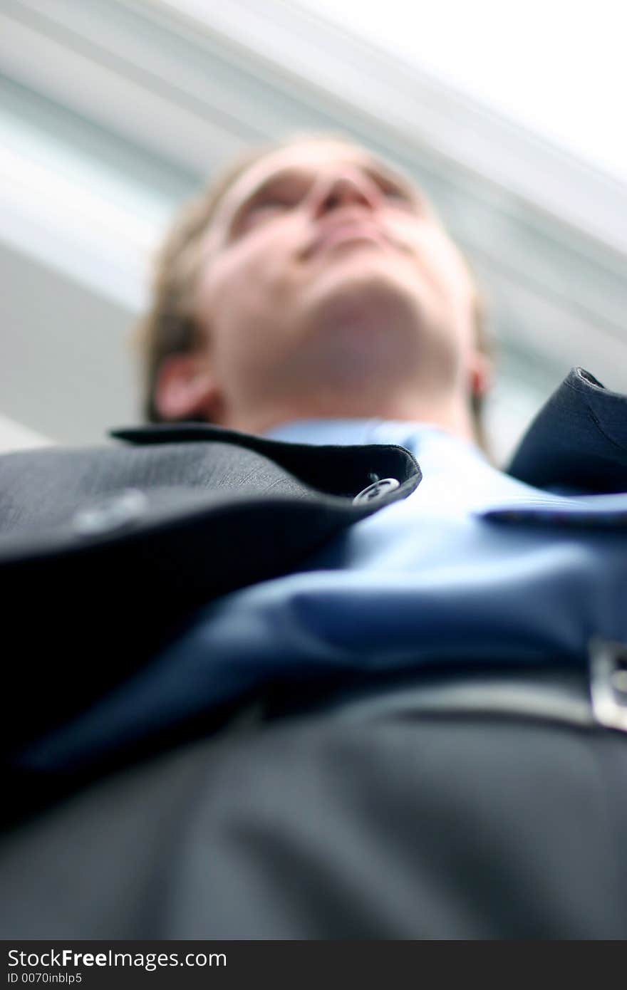 Business man in darker suit, blue shirt, and blue tie is posing in frornt of office building, shot from below. Business man in darker suit, blue shirt, and blue tie is posing in frornt of office building, shot from below