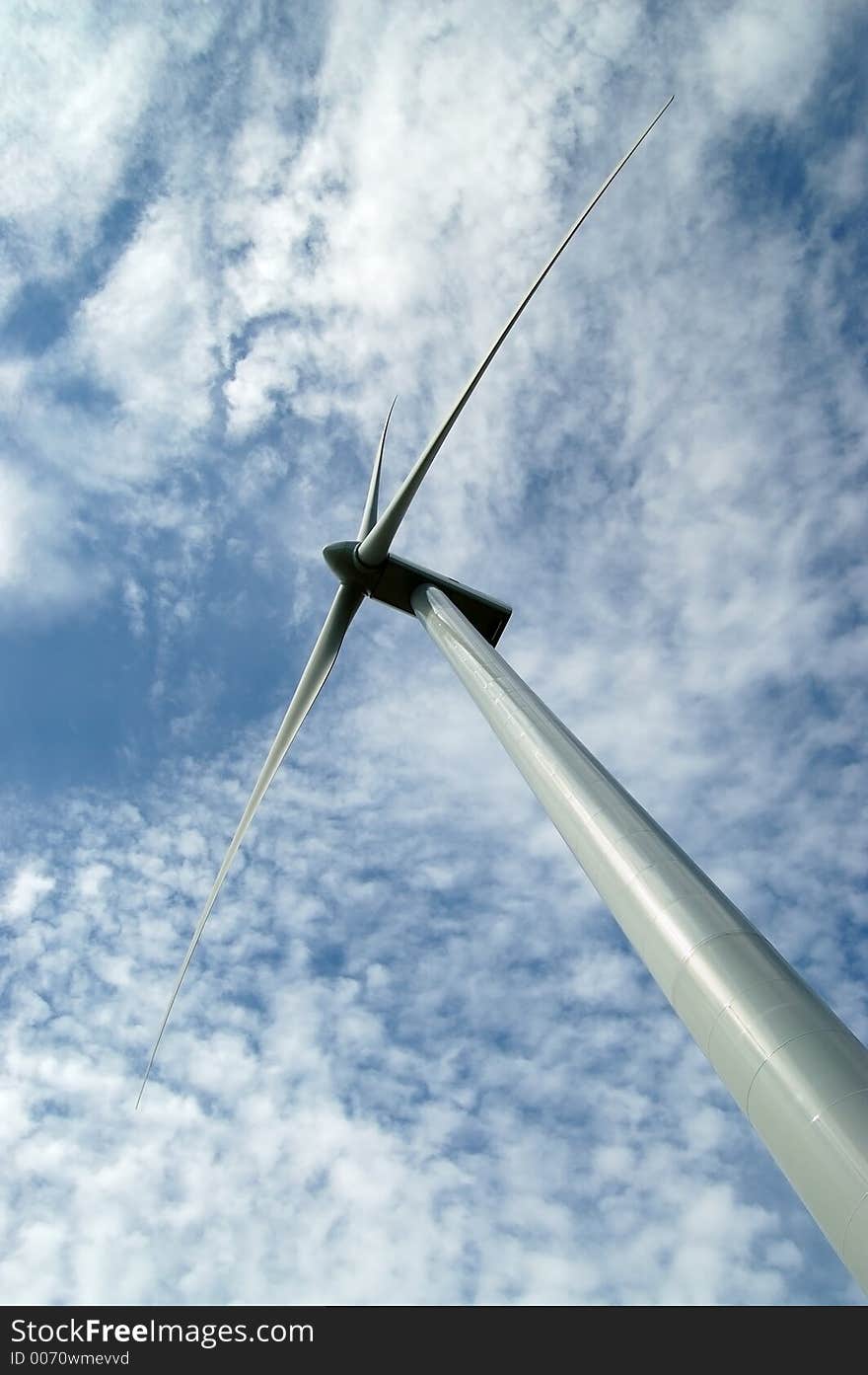 Looking up at a wind turbine set against a blue sky and clounds. Looking up at a wind turbine set against a blue sky and clounds