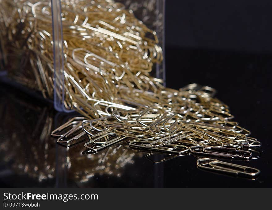 Box of gold paperclips on black background