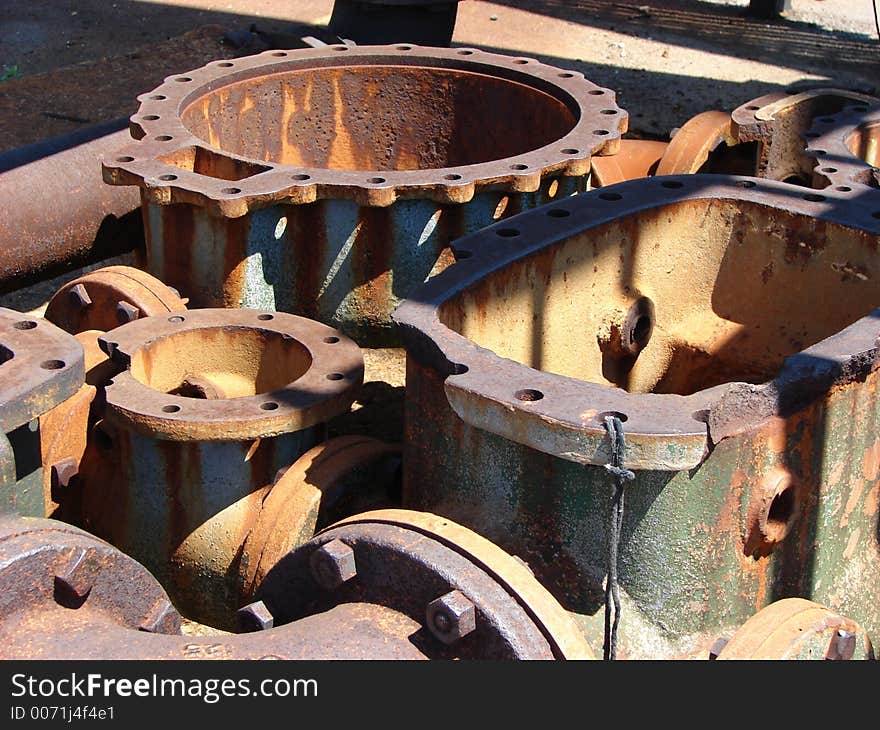 Pieces of old machinery which are rusted and have turned shades of orange, brown, and green and black. They are in the sunlight and there are dramatic shadows and highlights. Pieces of old machinery which are rusted and have turned shades of orange, brown, and green and black. They are in the sunlight and there are dramatic shadows and highlights.