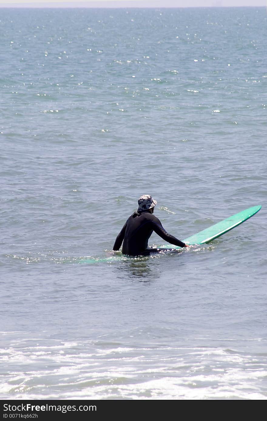 Surfer setting on green board waiting for next big wave. Surfer setting on green board waiting for next big wave.