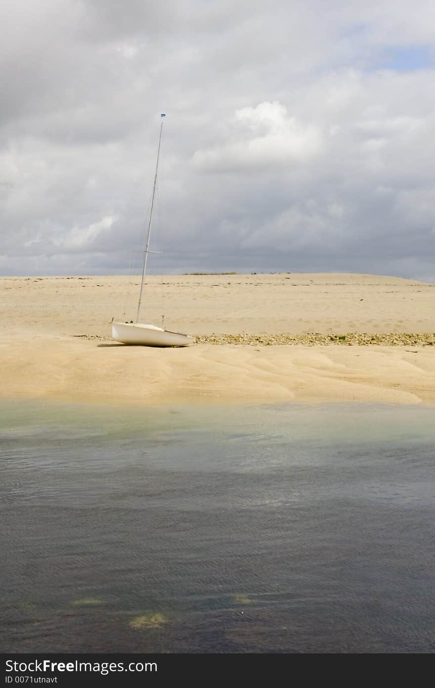 Yacht on remote island. Golden sands and blue seas under moody sky.