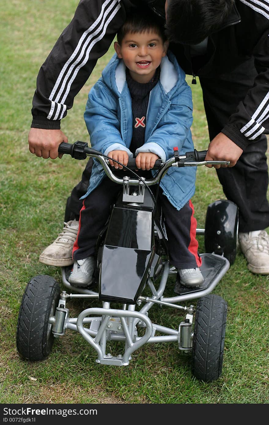 Little boy on a mini moto quad bike with an adult holding the handlebars and guiding the bike. Little boy on a mini moto quad bike with an adult holding the handlebars and guiding the bike.