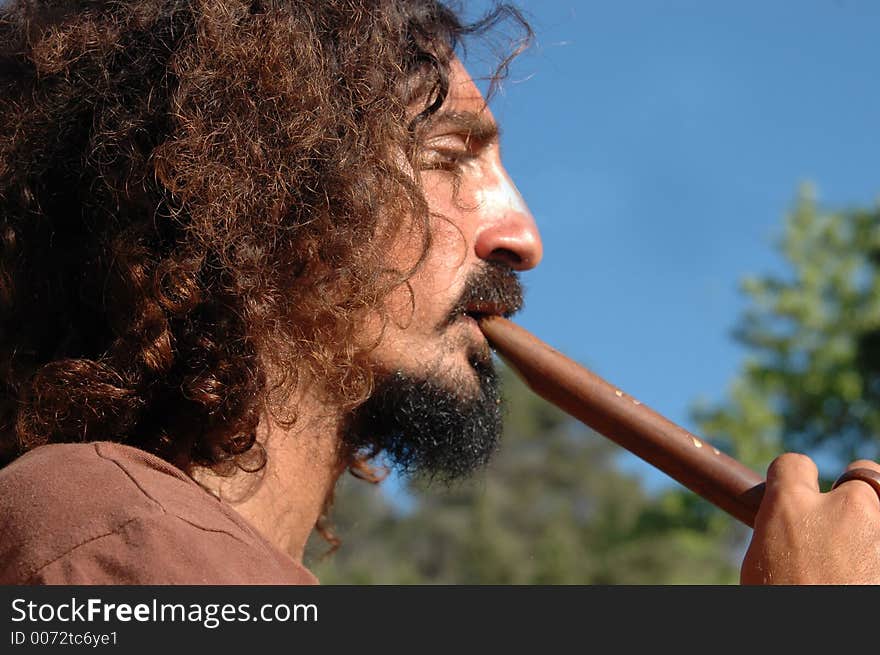 Men with long hippie hair playing the flute under a blue sky. Men with long hippie hair playing the flute under a blue sky