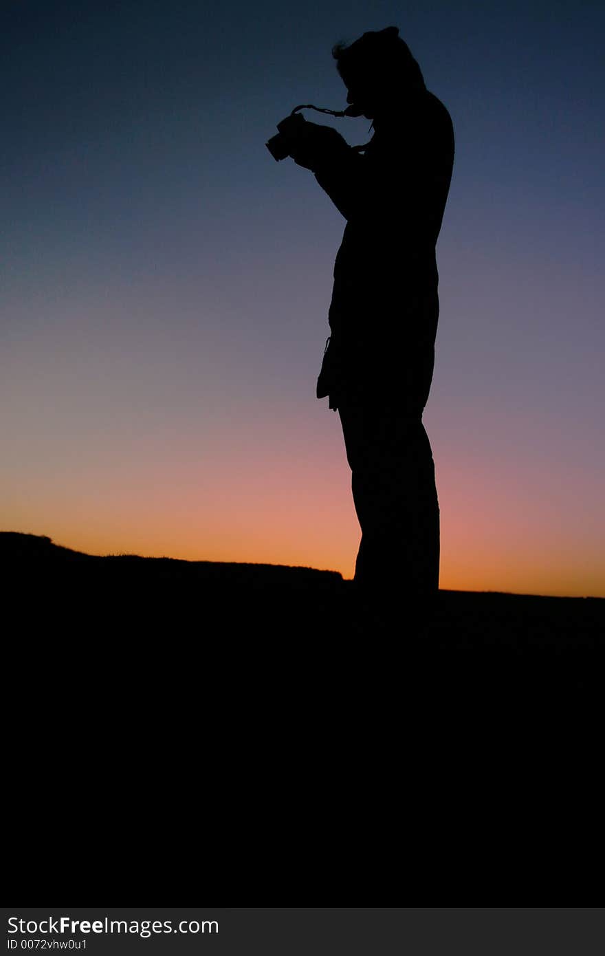 Silhouette female photographer at sunset taking pictures on a digital slr