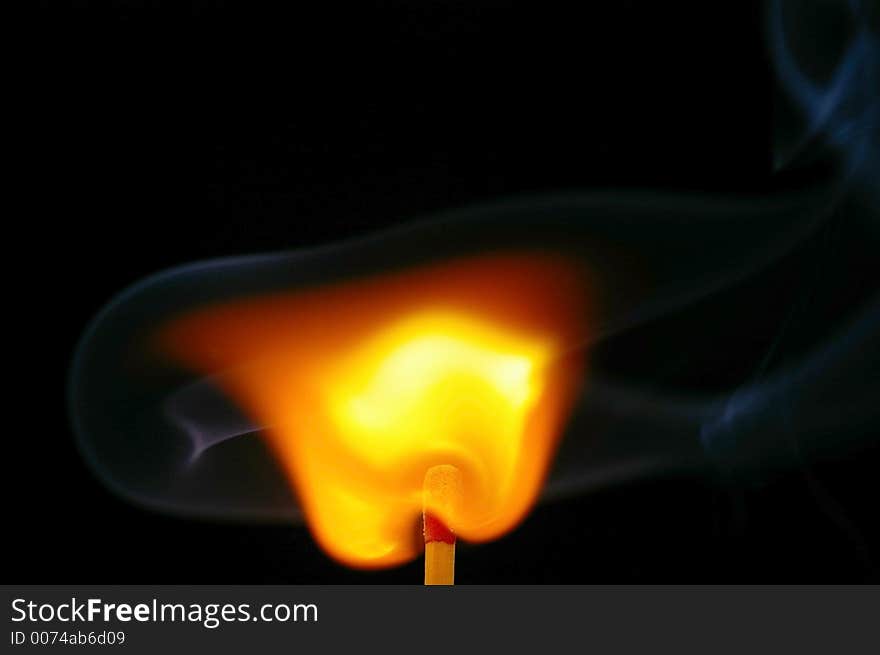 Closeup of a red-tipped wooden match stick at ignition with visible smoke.  Red, orange, yellow, and white flame.  Black background. Closeup of a red-tipped wooden match stick at ignition with visible smoke.  Red, orange, yellow, and white flame.  Black background.