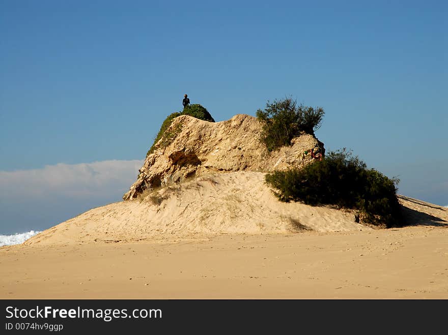 Man Standing On A Rocky Sand Dune Looking Out To Sea