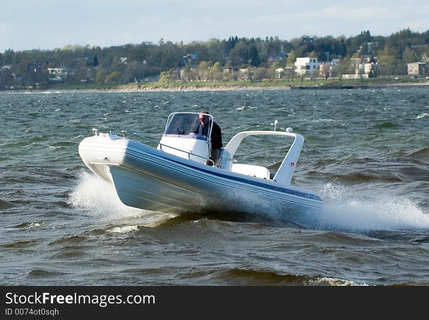 Modern lightweight speedboat speeding in the sea with the coastline visible nearby in the background. Modern lightweight speedboat speeding in the sea with the coastline visible nearby in the background.