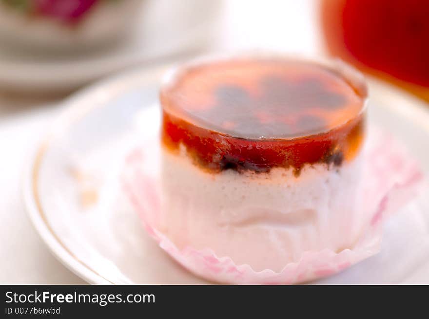 Mousse jelly cake with partially visible cup of tea and peach at blured background