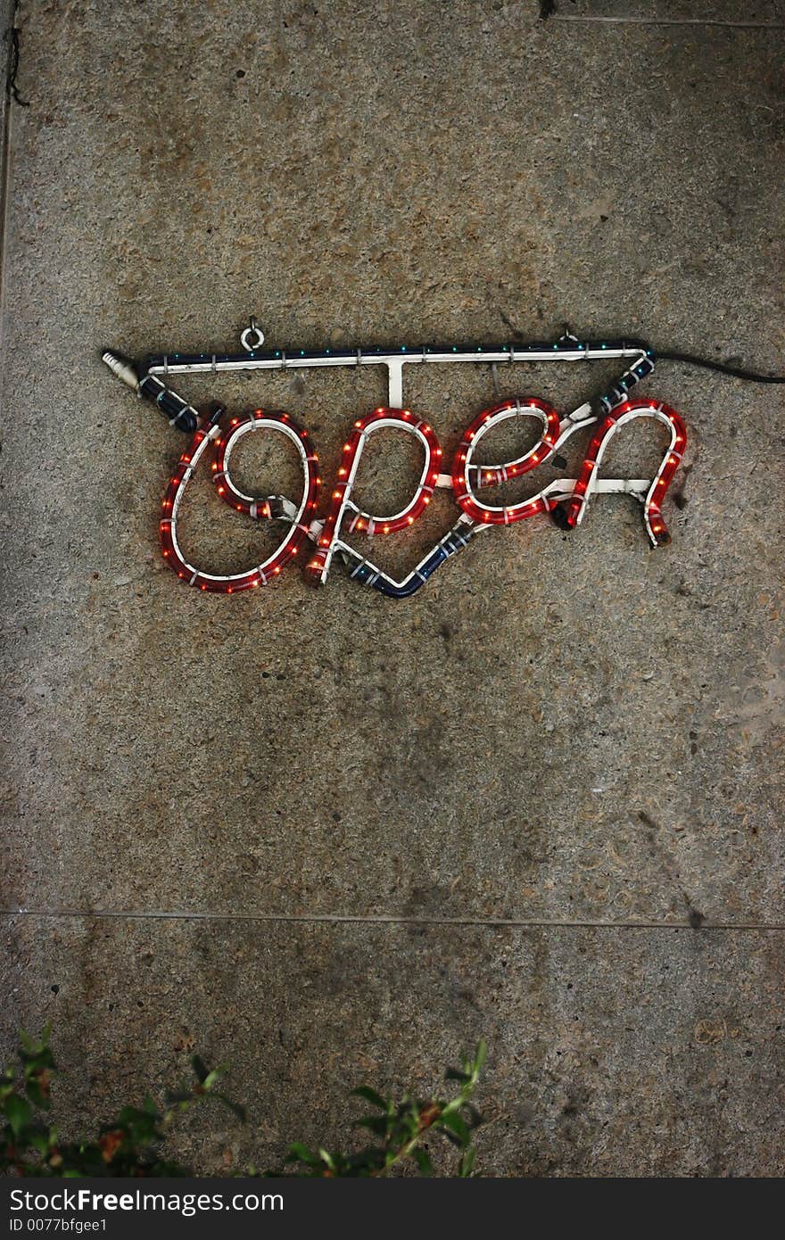 A neon open sign on a stone wall background.