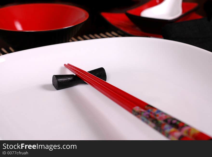 Red chopsticks on white plate with soup spoon and rice bowl