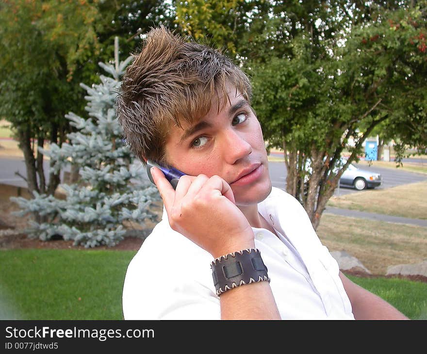 A young man looks at the camera while talking on his cell phone. A young man looks at the camera while talking on his cell phone