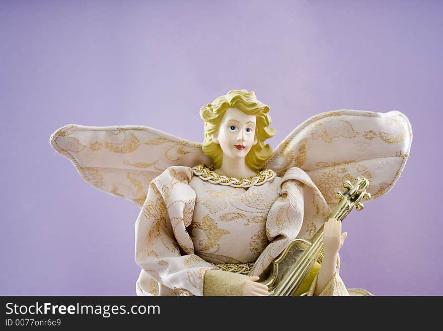 A lovely porcelain Christmas angel with blond hair and blue eyes in gold brocade holds a mandolin.