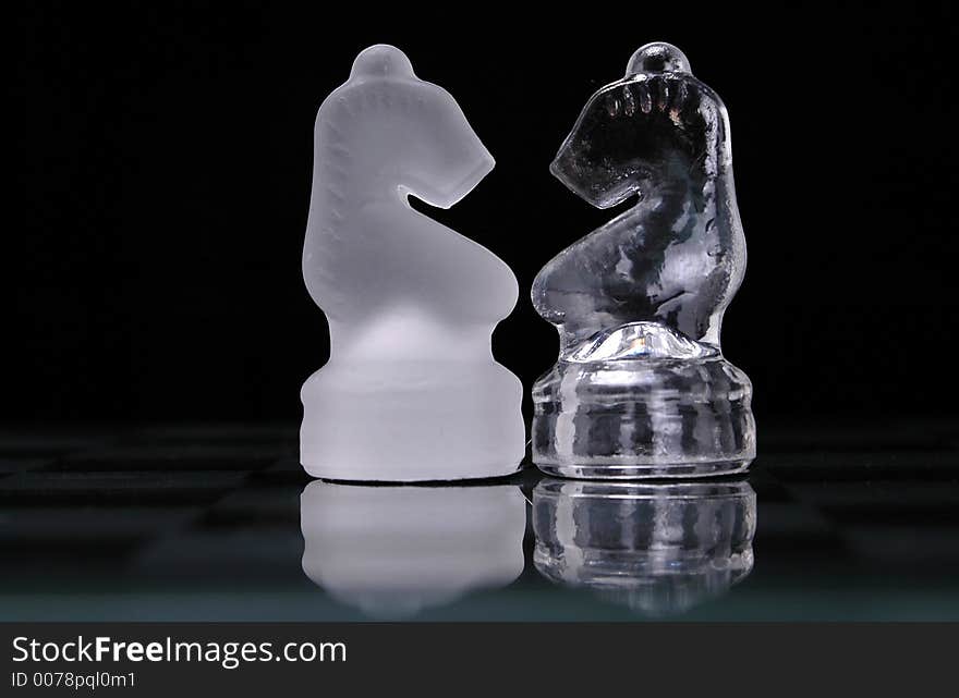 Opposing knights from a glass chess set face off.