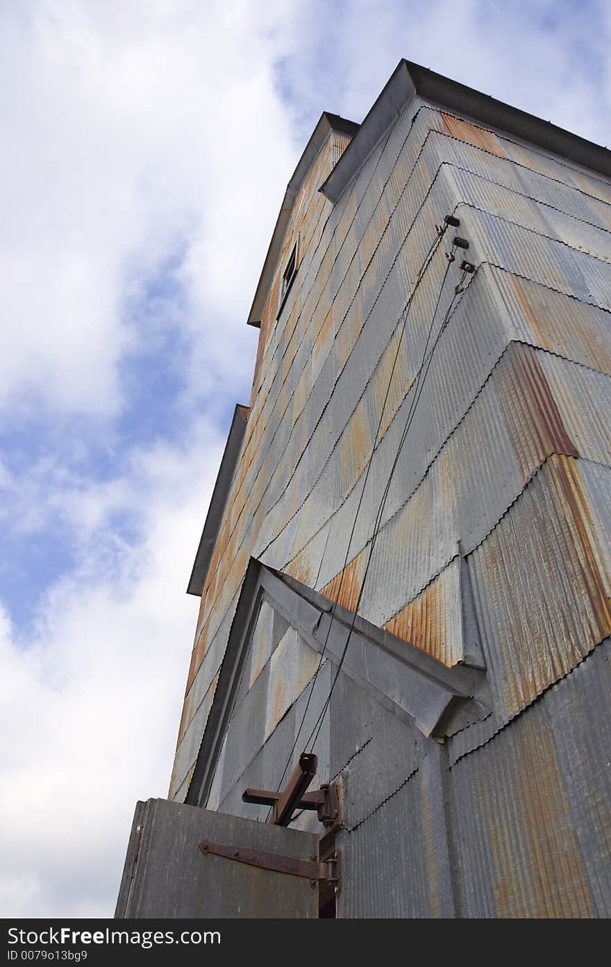 View looking up old rusted grain elevator - partly cloudy sky above. View looking up old rusted grain elevator - partly cloudy sky above