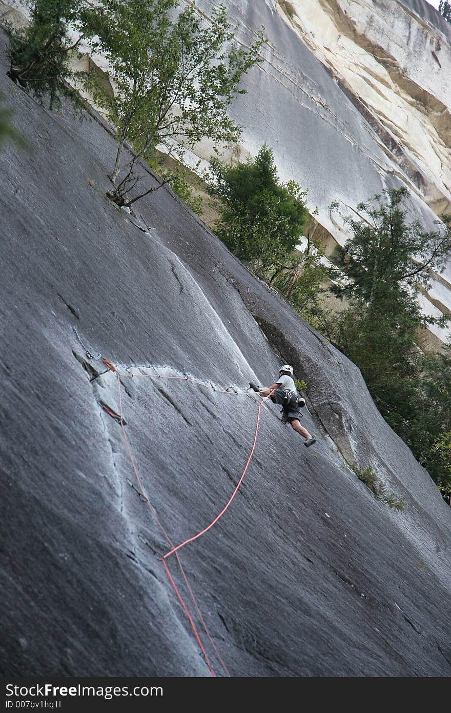 A rock climber working his way up a beautiful crack with a huge cliff face looming overhead. A rock climber working his way up a beautiful crack with a huge cliff face looming overhead.