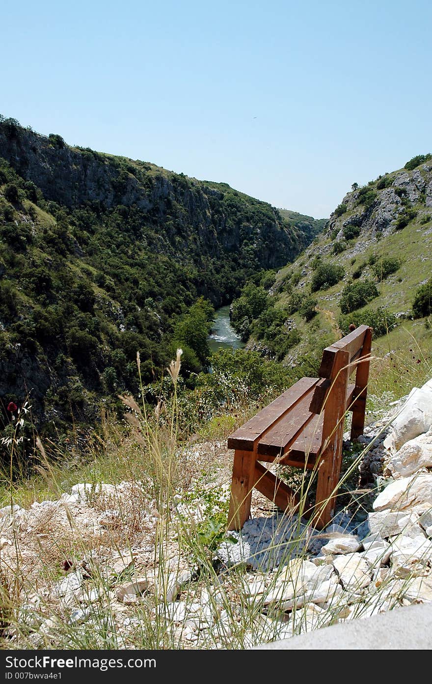 A wooden bench on the top of a hill and a river in the background. A wooden bench on the top of a hill and a river in the background