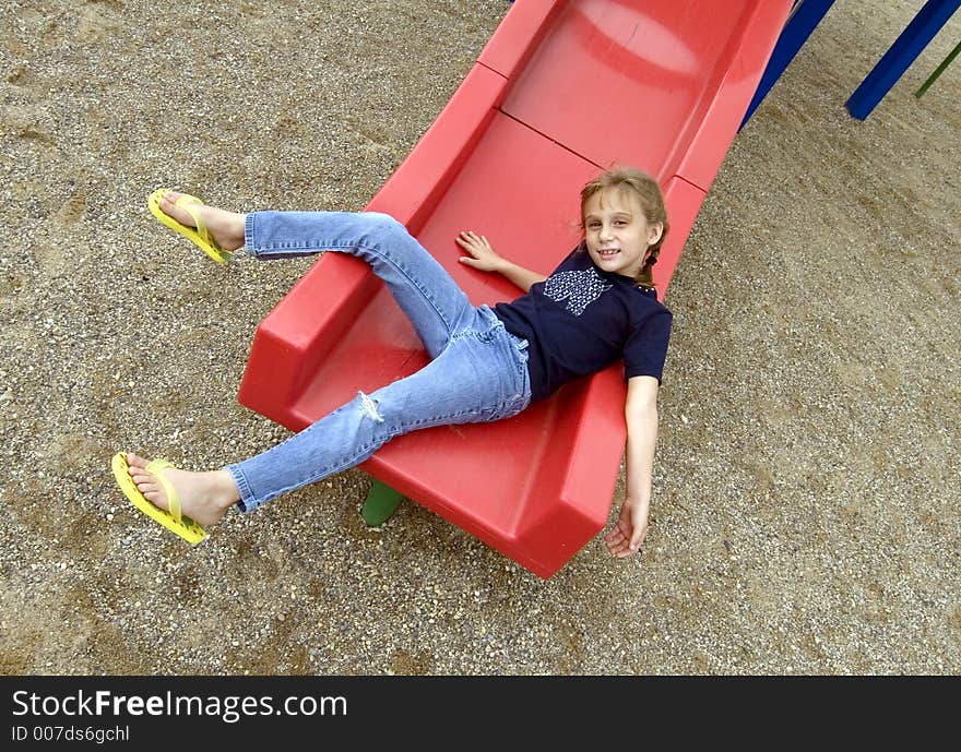 Young school girl poses on plastic slide during recess. Young school girl poses on plastic slide during recess