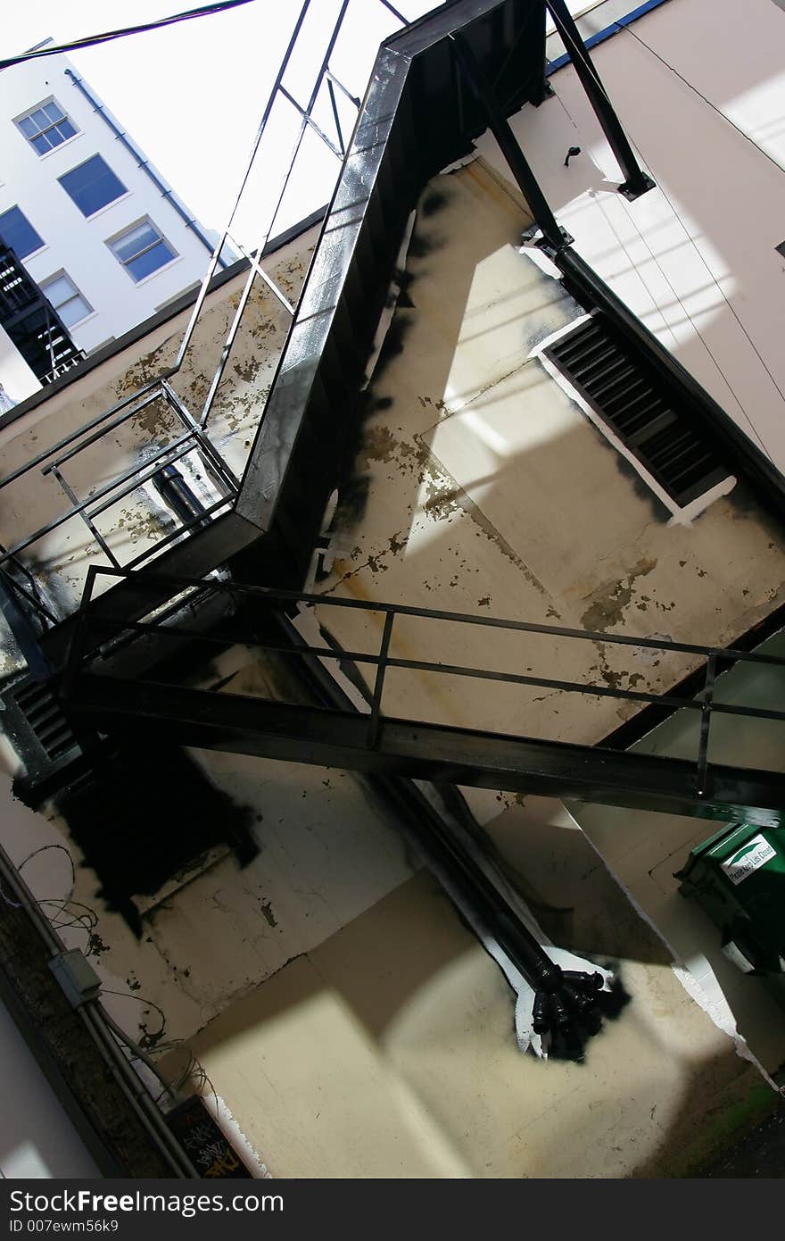 Old metal fire escape painted black against white cream colored wall in old back alley.