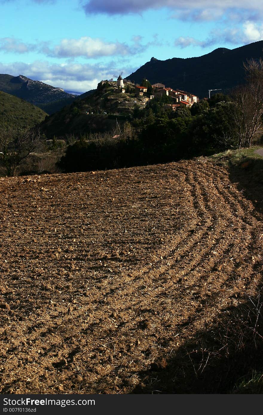 French village Cucugnan with a old mill on a hill and the ploughed ground on foreground.