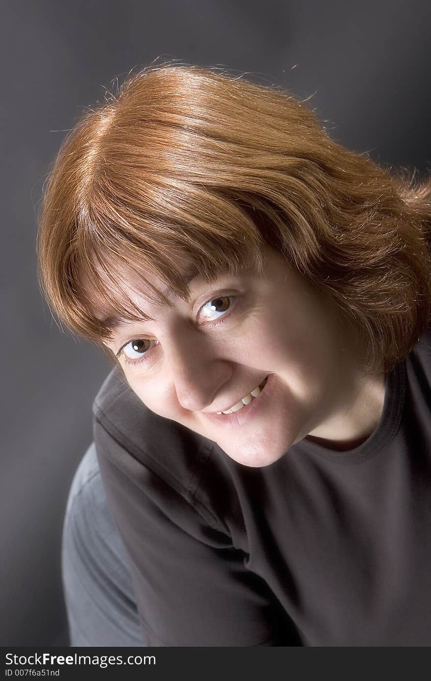 Female model with auburn hair looking into the camera, happy expression, against black background. Female model with auburn hair looking into the camera, happy expression, against black background