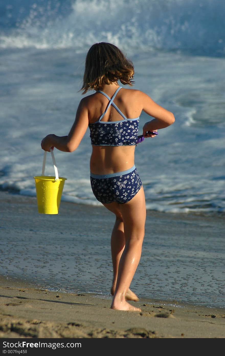 A girl is playing with sand on the beach near the water. A girl is playing with sand on the beach near the water