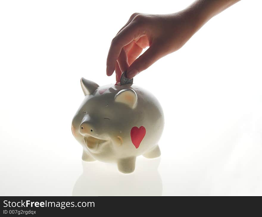 Piggy money-box on white background .a hand dropping a coin into a smiling piggy bank. Piggy money-box on white background .a hand dropping a coin into a smiling piggy bank