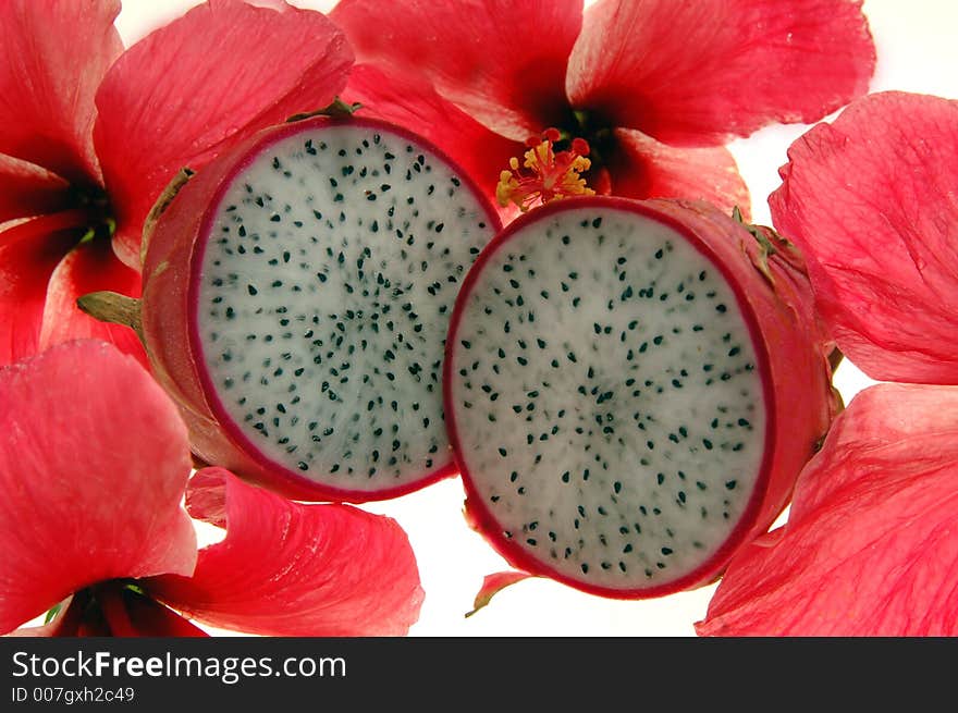 A sliced dragon fruit surrounded by pink hibiscus flowers on a white background. A sliced dragon fruit surrounded by pink hibiscus flowers on a white background