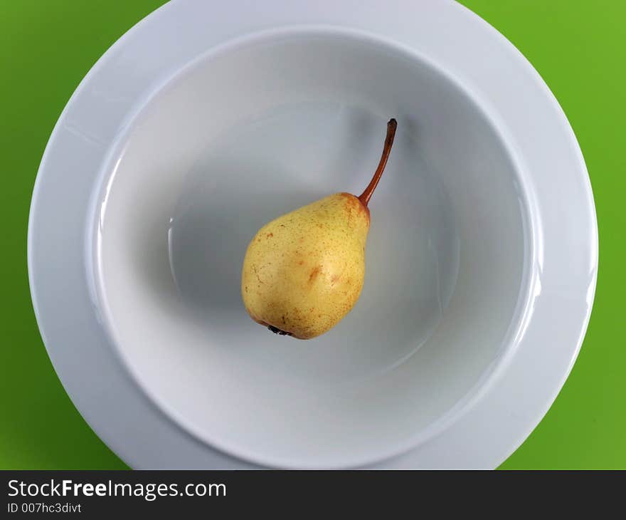 A very little yellow pear lays in a stilish porcelain plate. A plastic green table cloth is the background. A very little yellow pear lays in a stilish porcelain plate. A plastic green table cloth is the background