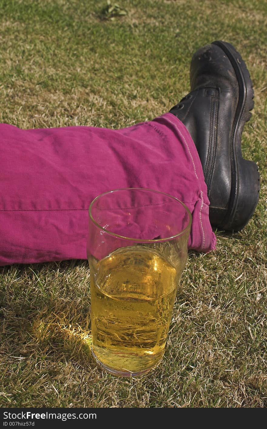 Pint of beer next to someone's leg on grass. Pint of beer next to someone's leg on grass