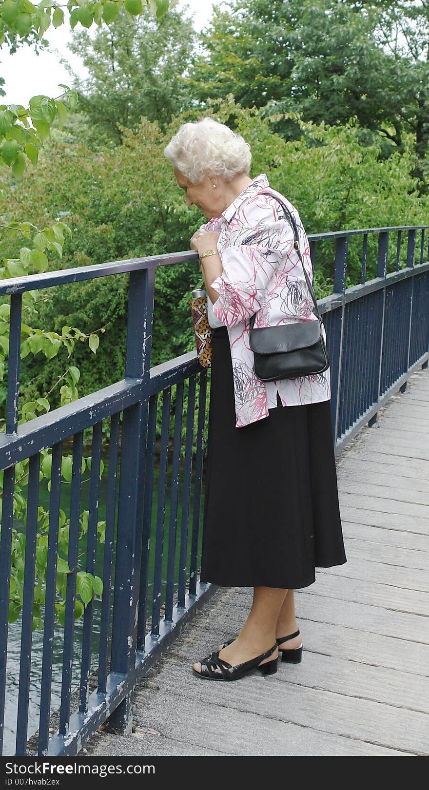 A 85 year old senior lady on a Sunday afternoon stroll in the park and looking into a river from a bridge. A 85 year old senior lady on a Sunday afternoon stroll in the park and looking into a river from a bridge