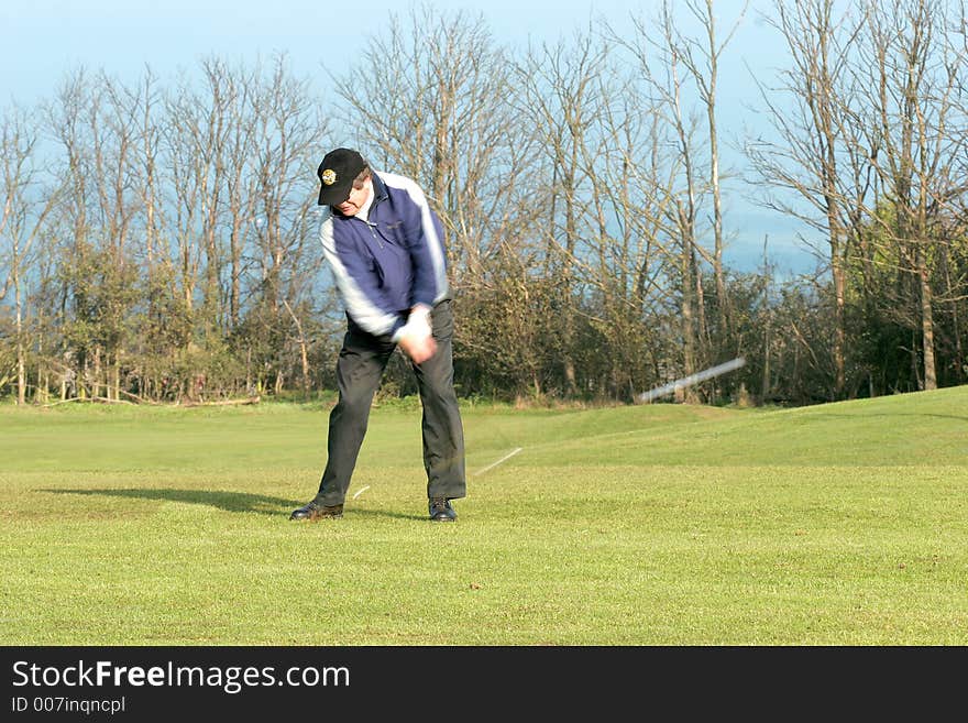 A golfer taking a shot and the ball is blurred