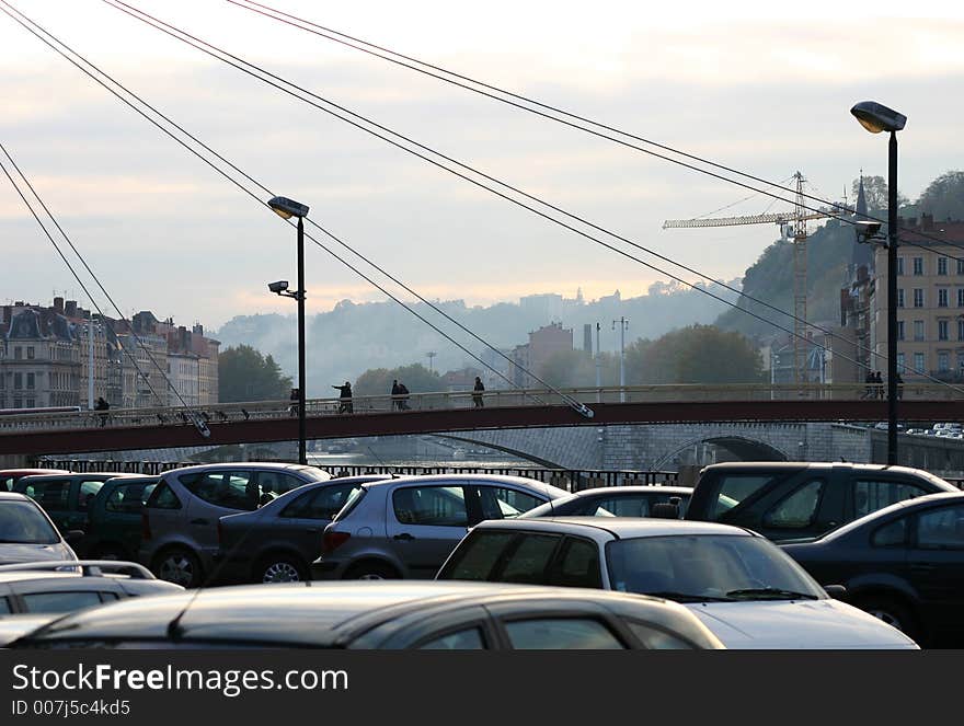 Lyon brigde with pedestrians on evening, car parking on foreground.