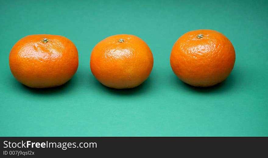 Three orange tangerines in a row on a contrasting and colourful green background. Three orange tangerines in a row on a contrasting and colourful green background.