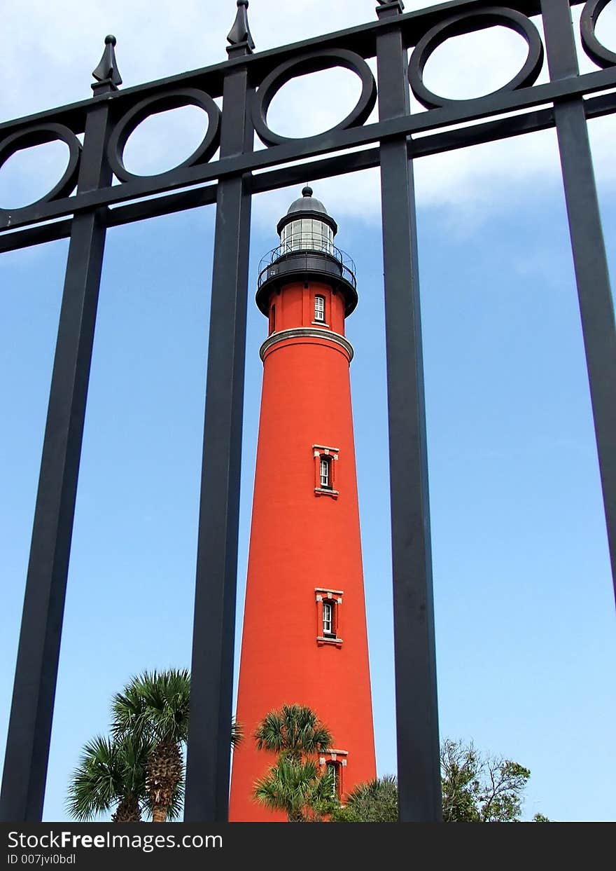 Red brick lighthouse in Ponce Inlet Florida framed by wrought iron fence. Red brick lighthouse in Ponce Inlet Florida framed by wrought iron fence.